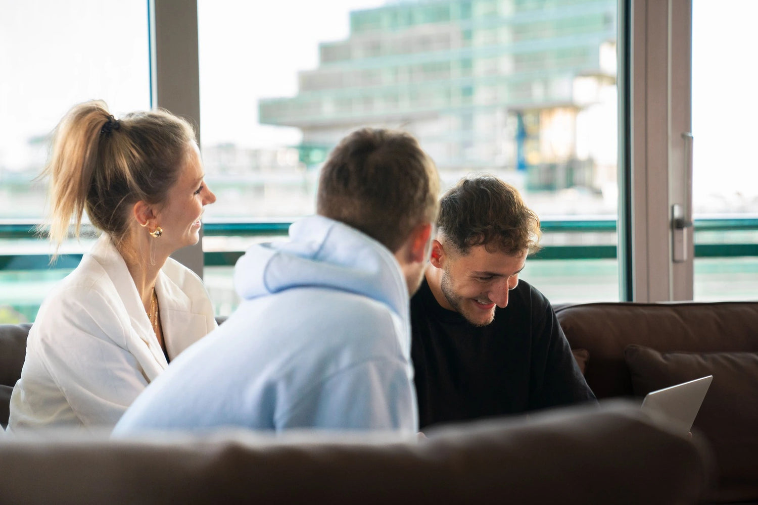 Drei Personen sitzen drinnen auf einem Sofa und sind um einen Laptop versammelt.
